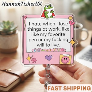 Può includere: Un porta badge quadrato in acrilico con una cornice rosa e una rana dei cartoni animati con un mantello rosso in alto. Il testo centrale recita: I hate when I lose things at work, like like my favorite pen or my fucking will to live. Include icone di cuori, stelle e una faccina sorridente.