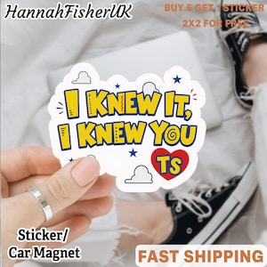 Könnte beinhalten: Ein gestanzter Aufkleber mit dem gelben Text I KNEW IT, I KNEW YOU TS und einem roten Herz. Das Design enthält blaue Sterne und weiße Wolkenumrisse auf weißem Hintergrund. Der Aufkleber wird vor einer weißen Stoffoberfläche gehalten.