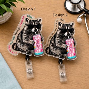 May include: Two acrylic badge reels featuring a raccoon wearing black sunglasses and holding a pink striped Alani energy drink can. The text reads I'M TRYING VERY HARD NOT TO BE A PROBLEM TODAY. Each badge reel has a clear plastic clip attachment.