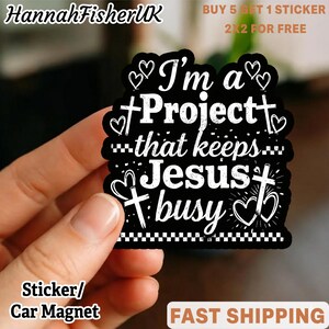 May include: Black sticker with white text that reads "I'm a Project that keeps Jesus busy." The sticker has a cross and heart design. The text "Sticker/Car Magnet" is at the bottom. The brand name "HannahFisherUK" is at the top.