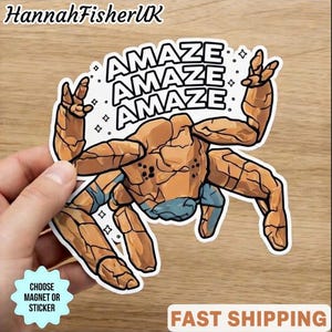 May include: A sticker featuring a cartoon character with the word "AMAZE" repeated three times. The character is primarily brown with blue accents and is making a hand gesture. The sticker has a white border and the text "CHOOSE MAGNET OR STICKER".