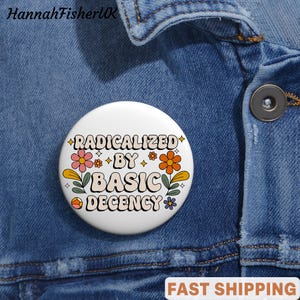 Może przedstawiać: Biała przypinka z napisem "RADICALIZED BY BASIC DECENCY" w stylu retro, otoczona kwiatowymi i gwiazdkowymi grafikami. Przypinka jest umieszczona na niebieskiej kurtce dżinsowej.