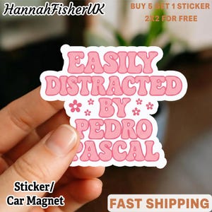 May include: A pink and white sticker with the text "EASILY DISTRACTED BY PEDRO PASCAL". The sticker also has small flower graphics. The sticker is a car magnet.
