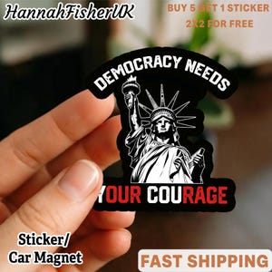 May include: Black sticker/car magnet featuring the Statue of Liberty with the text "DEMOCRACY NEEDS YOUR COURAGE" in white. The sticker also has the text "Sticker/Car Magnet" and the seller's name "HannahFisherUK".