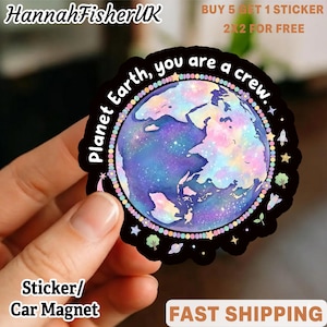 Op de afbeelding: Ronde sticker of auto-magneet met een kleurrijke illustratie van de aarde met een galaxy-ontwerp. De tekst "Planet Earth, you are a crew" staat rond de planeet. De sticker heeft een zwarte rand met kleine illustraties.