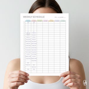 May include: A white weekly schedule planner with the text "WEEKLY SCHEDULE" at the top. The schedule is divided into days of the week with time slots for each day. The planner is held up by a person.