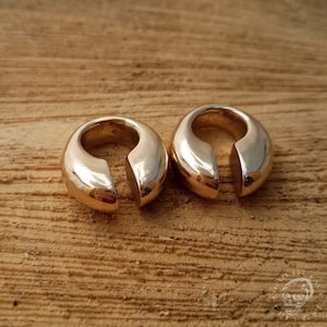 May include: Two gold-coloured metal ear cuffs with a rounded, open design. The cuffs are smooth and shiny.