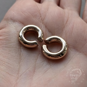 May include: Two gold-coloured hoop earrings, each with a smooth, rounded surface. The earrings are open on one side and have a slightly curved shape.