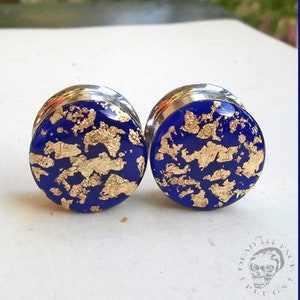 May include: A pair of blue and gold ear gauges with a silver metal rim. The gauges have a blue background with gold flakes scattered across the surface.