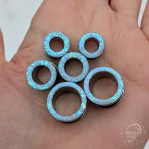 Un par de dilatadores de ópalo iridiscentes de color azul para orejas dilatadas. Dilatadores de purpurina de colores brillantes.
