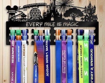 May include: Black metal medal display with a silhouette of a theme park and the text "EVERY MILE IS MAGIC". The display has multiple slots for hanging ribbons of various colors, with text on some ribbons.