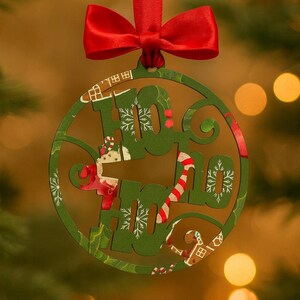 Op de afbeelding: Groene houten kerstbal met de woorden "HO HO HO" uitgesneden. Het heeft een rood lint en strik om op te hangen. Feestelijk ontwerp met sneeuwvlokken, zuurstokken en peperkoekhuisjes.