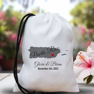 May include: White drawstring bag with a gray outline of Puerto Rico and a red star. The text "Puerto Rico" is written in black cursive script. The text "Gloria & Brian" and "November 4th, 2023" is written in black below the map.