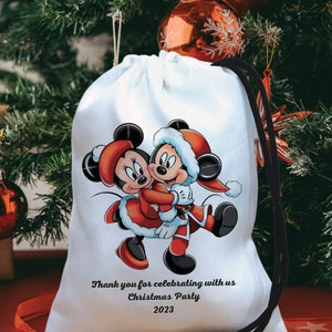 May include: White drawstring bag with a black drawstring. The bag features a colorful illustration of Mickey Mouse and Minnie Mouse dressed in Santa Claus outfits. The text "Thank you for celebrating with us Christmas Party 2023" is printed on the bag.