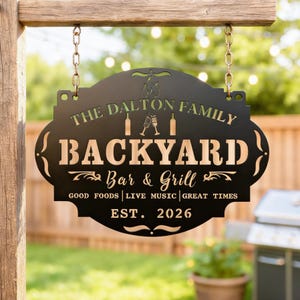 May include: Black metal sign with the text "THE DALTON FAMILY BACKYARD Bar & Grill" and "GOOD FOODS | LIVE MUSIC | GREAT TIMES EST. 2026". The sign is suspended from a wooden beam by chains. The background shows a garden.