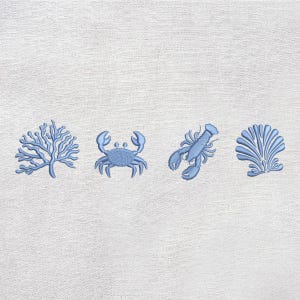 May include: Embroidered design with four light blue sea-themed motifs: coral, a crab, a lobster, and a seashell. The designs are stitched on white textured fabric, creating a nautical or coastal theme.