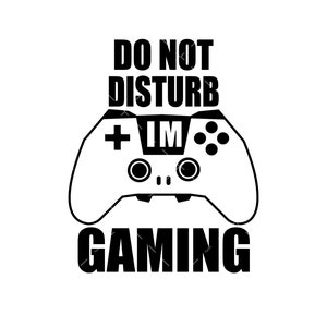 May include: Black and white graphic featuring a video game controller with the text "DO NOT DISTURB I'M GAMING". The controller has buttons and a directional pad. The text is in a bold, sans-serif font.