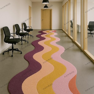 May include: A multi-coloured, wavy rug in a hallway. The rug has a design of alternating stripes in shades of purple, peach, yellow, and pink. Black chairs line the wall, and black pendant lights hang from the ceiling.