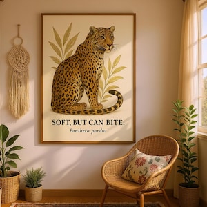 Puede incluir: Un cuadro enmarcado con una ilustración detallada de un leopardo sobre un fondo crema con detalles botánicos. El texto "SOFT, BUT CAN BITE" y "Panthera pardus" están impresos debajo. La impresión se muestra en una habitación.