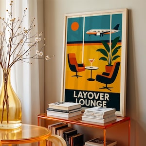 May include: A framed art print featuring a retro-style illustration of an airport lounge. The artwork depicts an airplane in flight, a sun, and lounge chairs. The words "LAYOVER LOUNGE" are printed at the bottom. The print is displayed on a wall next to a vase and books.