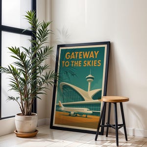 May include: A framed poster with the text "Gateway to the Skies" features a vintage airport design. The artwork includes an airplane, control tower, and terminal building in shades of teal, orange, and beige. A wooden stool with black legs sits nearby.