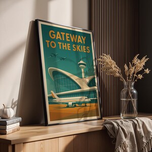 May include: Framed art print featuring a vintage-style illustration of an airport terminal with the text "Gateway to the Skies." The artwork showcases an airplane on the tarmac, with a teal and orange color scheme. The print is displayed on a wooden surface.