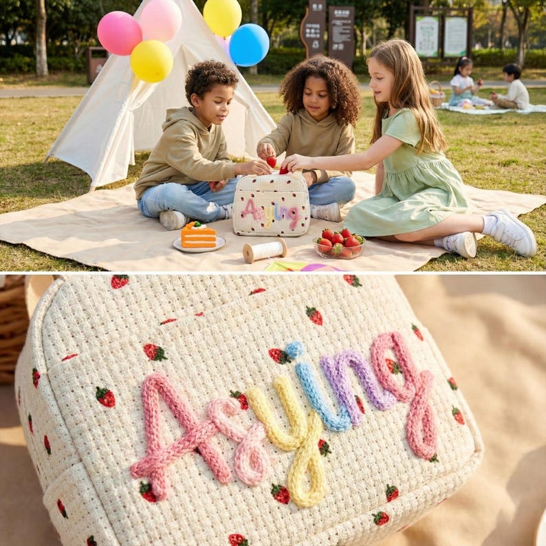 May include: A cream-colored picnic basket with a strawberry pattern and the name "Aying" embroidered in pink, blue, and yellow. The basket is surrounded by children, a tent, balloons, and food, suggesting a picnic setting.