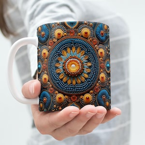 Könnte beinhalten: Eine weiße Keramiktasse mit einem blauen, goldenen und orangefarbenen Mandala-Design. Das Mandala ist aufwendig und detailliert mit einer Vielzahl von geometrischen Formen und Mustern.