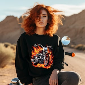 May include: A black sweatshirt with a graphic of a motorcycle engulfed in flames. The motorcycle is silver and black with a red seat. The flames are orange and yellow.