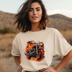 May include: A cream colored t-shirt with a graphic of a motorcycle engulfed in flames. The motorcycle is black and red with a chrome headlight.