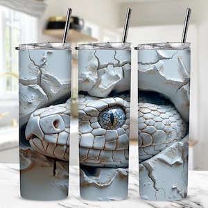 Può includere: Tre bicchieri in acciaio inossidabile con un design a serpente bianco. L'occhio del serpente è blu e il serpente è parzialmente nascosto dietro una superficie bianca screpolata.