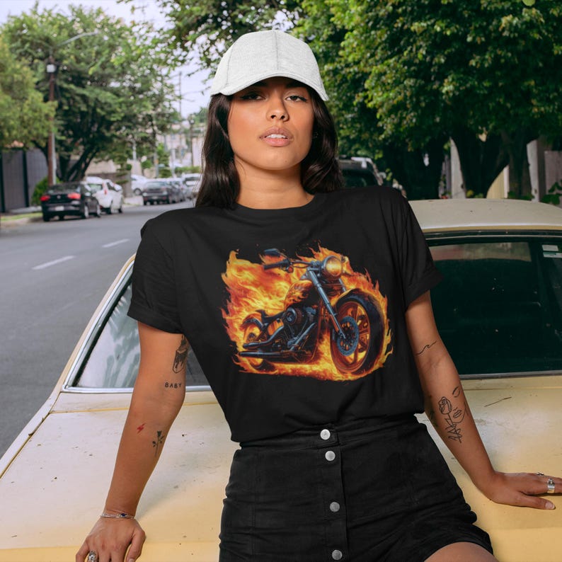 Puede incluir: Una camiseta negra con un gr&aacute;fico de una motocicleta envuelta en llamas. La motocicleta es negra y tiene un tubo de escape cromado. Las llamas son de color naranja y amarillo.