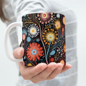 May include: A white ceramic mug with a black background and a colorful floral pattern. The flowers are red, yellow, blue, and green. The mug has a white handle.