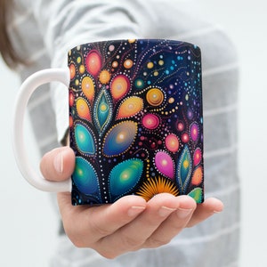 May include: A white ceramic mug with a black background and colorful abstract floral design. The design features a variety of colors, including pink, blue, green, yellow, and orange.