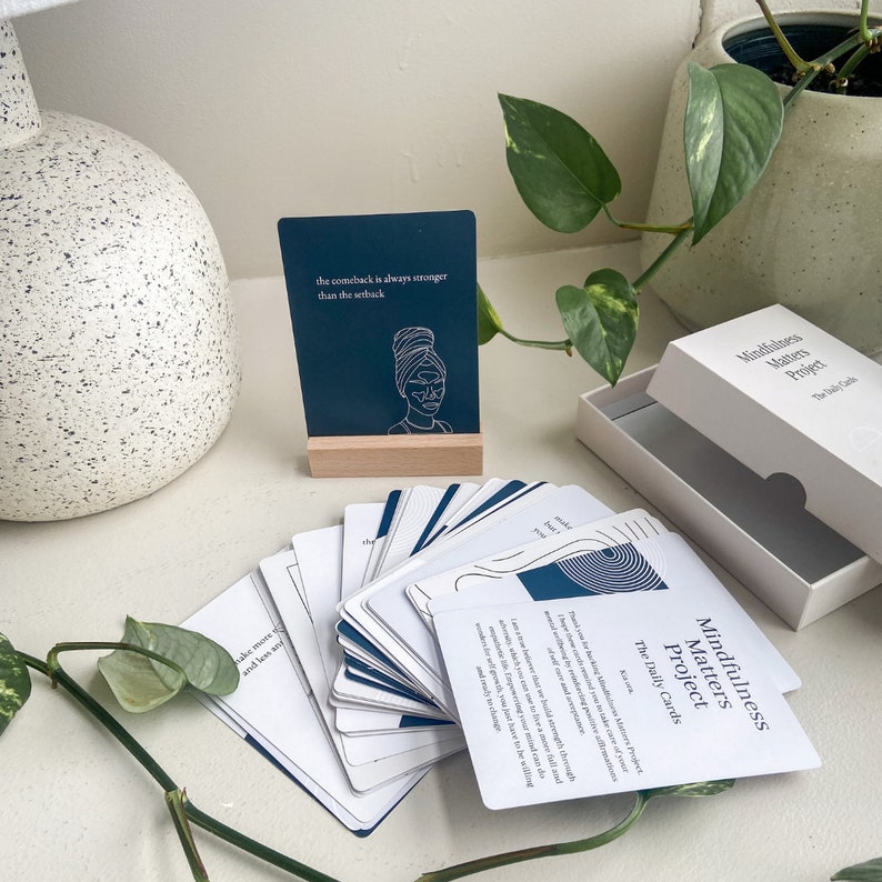May include: A deck of Mindfulness Matters Project daily cards with a blue and white design. The cards are fanned out on a white surface. The top card reads "Mindfulness Matters Project The Daily Cards".