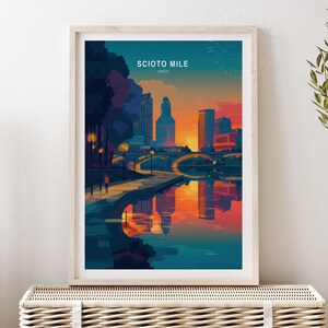 May include: A framed art print titled "Scioto Mile" depicts a colorful cityscape at sunset. The artwork features a river reflecting the buildings and sky in shades of orange, blue, and purple. The print is displayed on a woven chest.