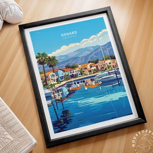 May include: A framed art print featuring a vibrant illustration of Oxnard, California. The artwork depicts a harbor scene with boats, houses, palm trees, and mountains under a blue sky. The print is in a black frame and is displayed on a wooden surface.