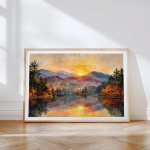 Puede incluir: Una impresión de paisaje enmarcada que muestra un atardecer sobre una cordillera y un lago tranquilo. La escena presenta tonos de cielo naranja y amarillo, montañas con tonos púrpuras y pinos verde oscuro, con un reflejo claro en el agua.
