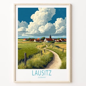 May include: A framed art print of a rural landscape with a winding dirt path leading to a village. The artwork features a bright blue sky with fluffy white clouds, green fields, and red-roofed buildings. The text "LAUSITZ GERMANY" is at the bottom.