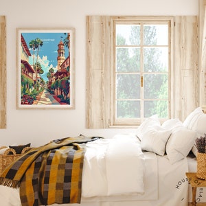 May include: A framed print of a colorful illustration of a street scene in St. Augustine, Florida. The print is hanging on a white wall above a bed with a white duvet and a yellow and black plaid throw blanket.