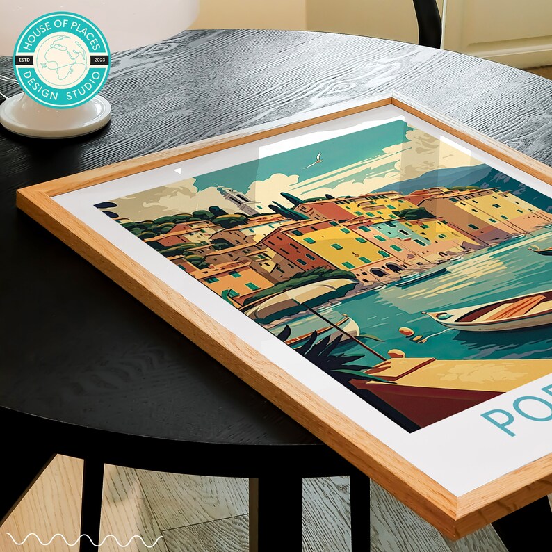 May include: A framed print of a colorful illustration of a seaside town with buildings, boats, and palm trees. The print has the text "Portofino" at the bottom.