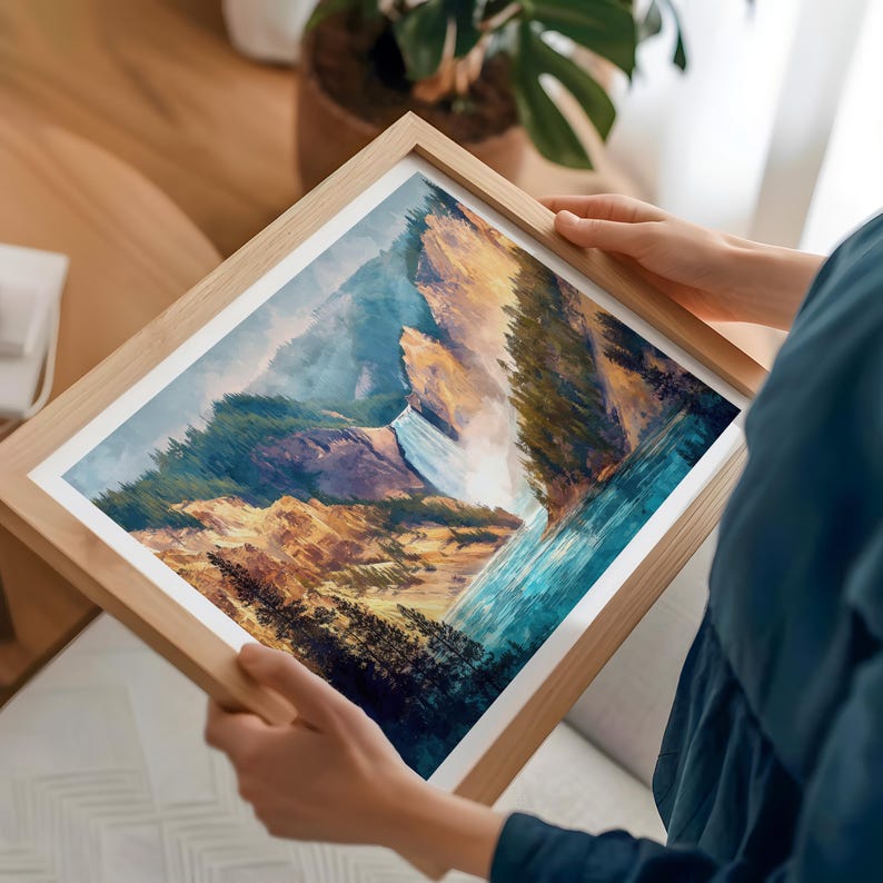 Op de afbeelding: Een ingelijste kunstdruk met een waterval die van een rotsachtige berg naar beneden stort. Het kunstwerk gebruikt tinten blauw, groen en bruin. Het frame is gemaakt van lichtgekleurd hout.