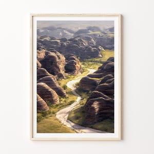 Puede incluir: Impresión enmarcada de un paisaje que muestra un camino sinuoso a través de un cañón. La obra de arte presenta formaciones rocosas en capas en tonos marrones y grises, con parches de vegetación verde y un camino claro.