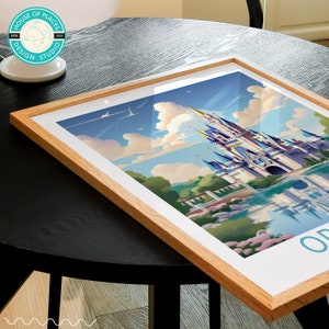 May include: A framed print of a colourful illustration of Cinderella's Castle at Walt Disney World in Orlando, Florida. The castle is surrounded by lush greenery and a blue lake. The print is in a light wood frame.