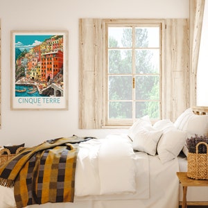 K&ouml;nnte beinhalten: Ein Schlafzimmer mit einem wei&szlig;en Bett, einem h&ouml;lzernen Kopfteil und einem Fenster mit Blick auf B&auml;ume. Ein gerahmtes Poster mit einer farbenfrohen Illustration des italienischen Dorfes Cinque Terre h&auml;ngt an der Wand &uuml;ber dem Bett. Ein geflochtener Korb mit Lavendelbl&uuml;ten steht auf einem h&ouml;lzernen Beistelltisch.