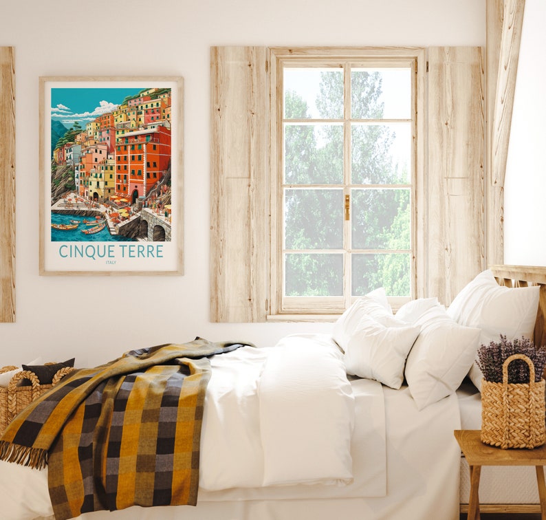 K&ouml;nnte beinhalten: Ein Schlafzimmer mit einem wei&szlig;en Bett, einem h&ouml;lzernen Kopfteil und einem Fenster mit Blick auf B&auml;ume. Ein gerahmtes Poster mit einer farbenfrohen Illustration des italienischen Dorfes Cinque Terre h&auml;ngt an der Wand &uuml;ber dem Bett. Ein geflochtener Korb mit Lavendelbl&uuml;ten steht auf einem h&ouml;lzernen Beistelltisch.