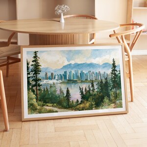 May include: A framed landscape print featuring a watercolour-style cityscape across a body of water, framed by dark green evergreen trees in the foreground and soft blue mountains in the distance under a pale sky with light clouds.