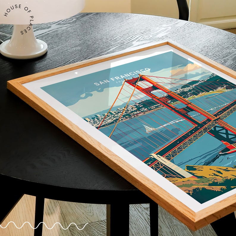 May include: A framed print of a colourful illustration of the Golden Gate Bridge in San Francisco, California. The bridge is red and the water is blue. The city skyline is visible in the background.