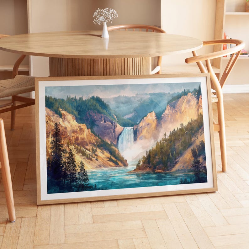 Op de afbeelding: Een ingelijste aquarelprint van een schilderachtige waterval die in een turquoise rivier stort, omgeven door weelderige groene bomen en torenhoge rotsformaties. Het kunstwerk wordt op een houten vloer getoond.