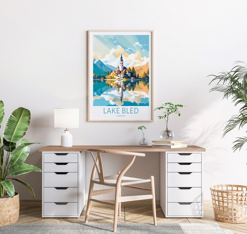 Op de afbeelding: Een minimalistisch thuiskantoor met een wit bureau en een houten stoel. Een ingelijst poster met een kleurrijke illustratie van het meer van Bled, Sloveni&euml;, hangt aan de muur boven het bureau. De poster luidt "Lake Bled, Sloveni&euml;".